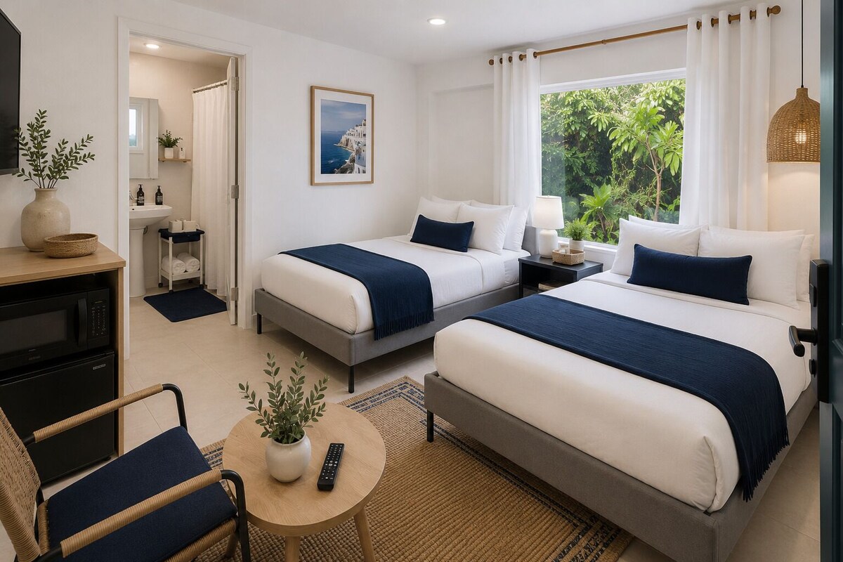 A hotel room with two beds, a desk, a chair, a small table with a plant, and a window with curtains.