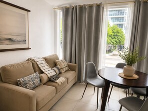 Sala de estar com sofá, cadeiras, mesa e janela com cortinas.