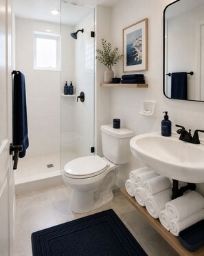 A modern bathroom with a glass shower enclosure, a white toilet, a white sink, and neatly rolled towels. - Beautiful Deluxe Queen Room (Fort Lauderdale)