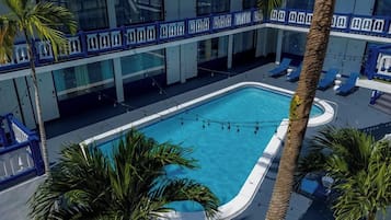 Un área de piscina con sillones de descanso y palmeras.