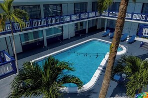 Un área de piscina con sillones de descanso y palmeras.