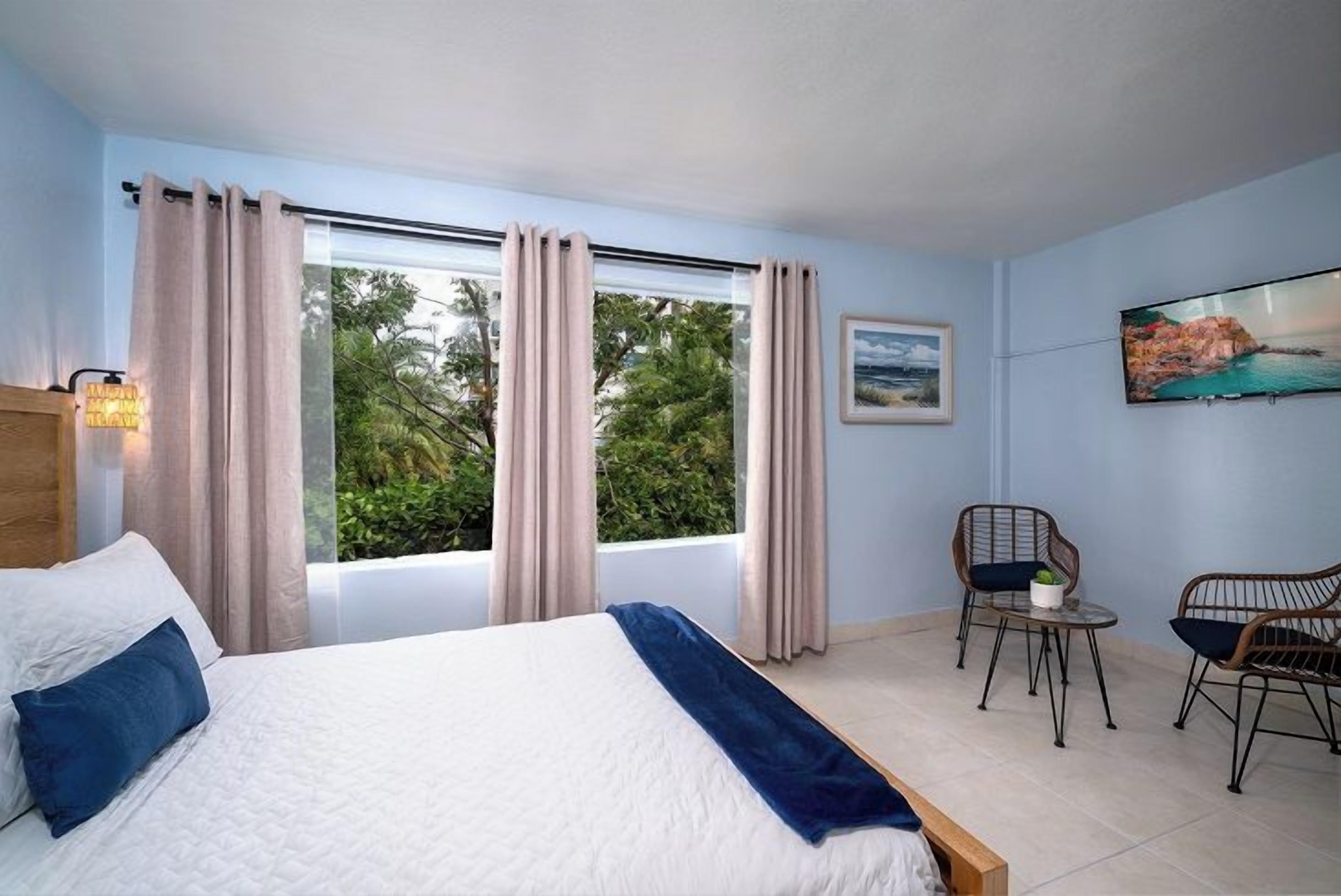 A bedroom with a bed, two chairs, a small table, and a window with curtains.