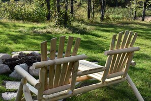 Two wooden Adirondack chairs in a grassy outdoor area with a fire pit in the background. - Hayward Northwoods Escape -ATV Trails, Pond + Kayaks & Firepit (Hayward)