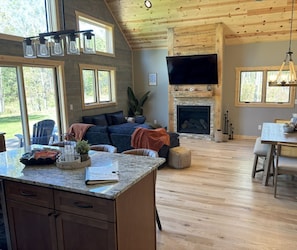 A spacious living area with a fireplace, a television mounted above it, and a dining area with a table and chairs.