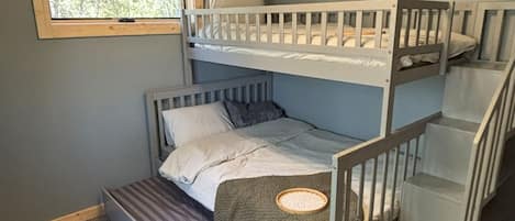 A bunk bed room with a window, carpeted floor, and a staircase.