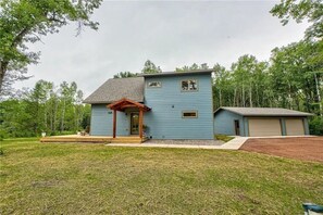 A two-story house with a porch, a garage, and a well-maintained lawn. - Hayward Northwoods Escape -ATV Trails, Pond + Kayaks & Firepit (Hayward)