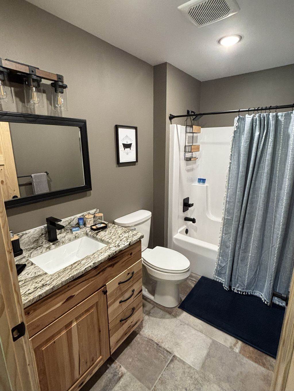 Une salle de bain avec un lavabo en marbre, un meuble-lavabo en bois, des toilettes blanches et une douche avec un rideau.