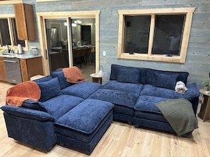 A blue sectional sofa with a dog, a small table, and a window with wooden frames.