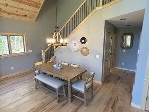 A dining area with a wooden table, benches, and a chandelier. - Hayward Northwoods Escape -ATV Trails, Pond + Kayaks & Firepit (Hayward)