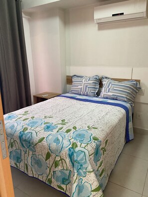 A bedroom with a bed, a nightstand, a wall-mounted air conditioning unit, and a curtain. - 2802 Unique Estudio Caragem (Belem)