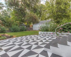 A geometric patterned patio with steps leading to a white structure, surrounded by greenery and a house in the background. - Serene 2-bedroom near Tulsa Expo Home, sleeps 6, fenced yard (Tulsa)