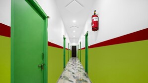 Um corredor com paredes verdes e vermelhas, um extintor fixado na parede e um chão estampado.