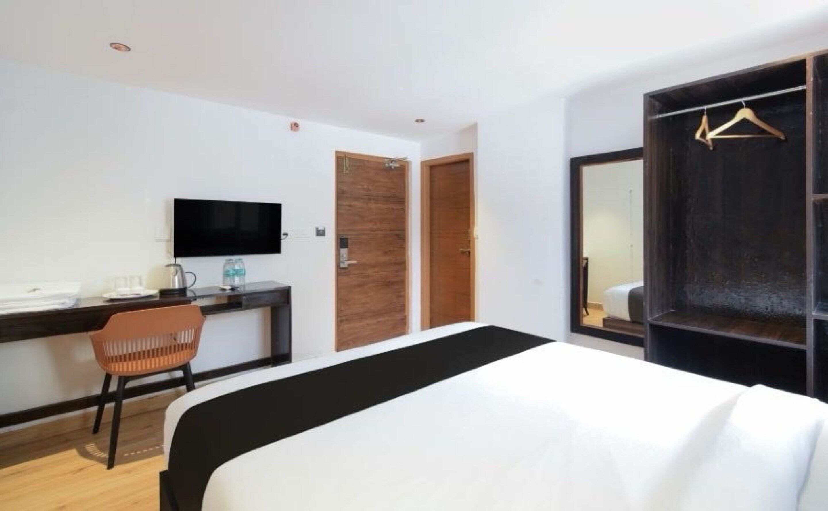 A hotel room with a bed, a desk with a chair, a television, and a wardrobe with a mirror.
