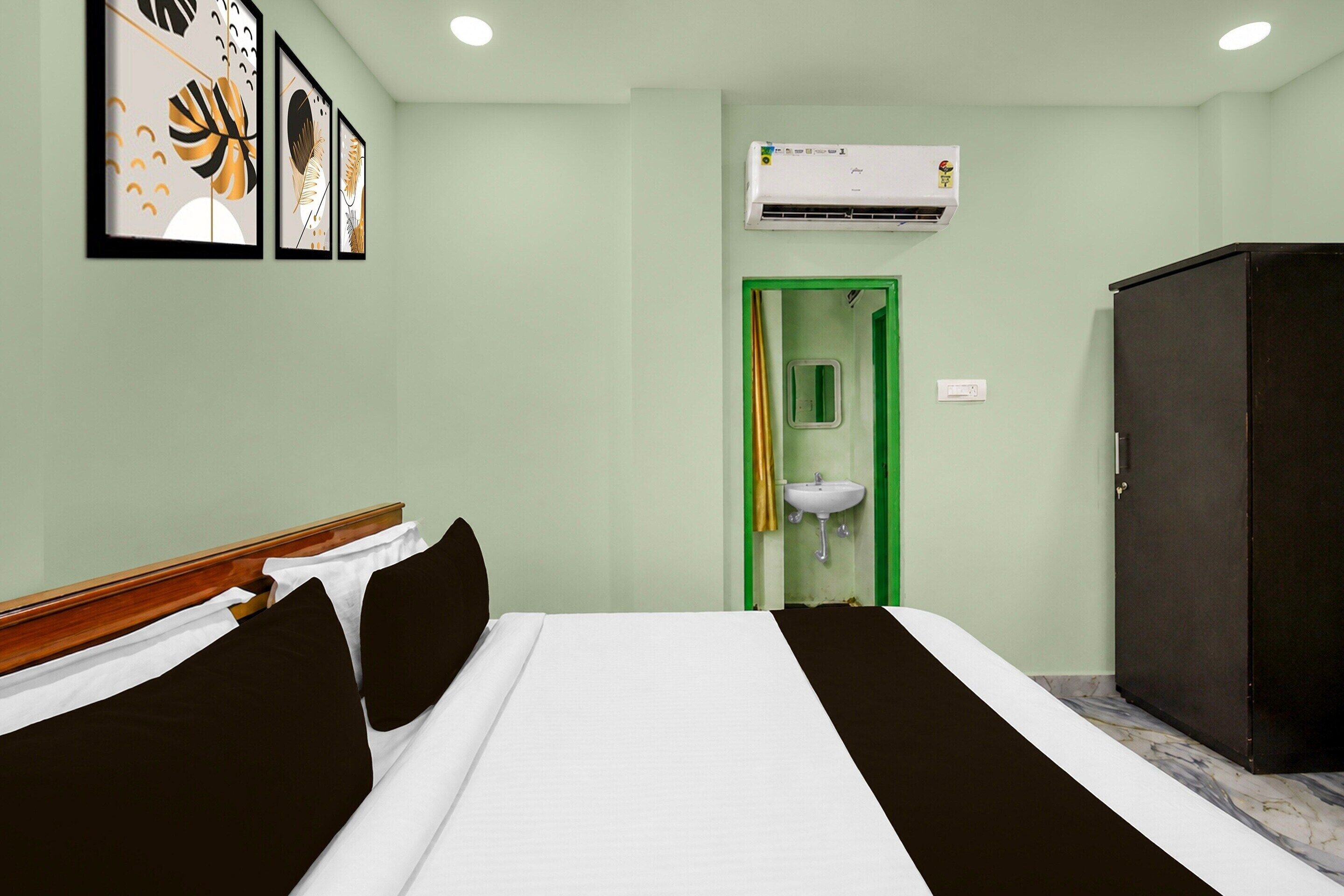 A hotel room with a bed, a wardrobe, a sink, and an air conditioning unit.