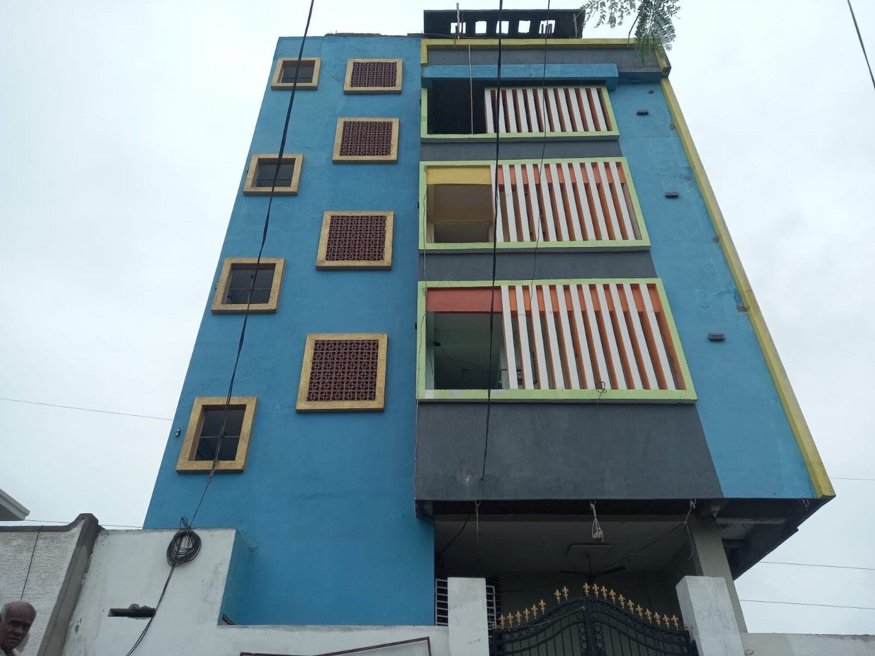Un edificio a più piani con facciata blu, numerose finestre con persiane e un ingresso chiuso da cancello.