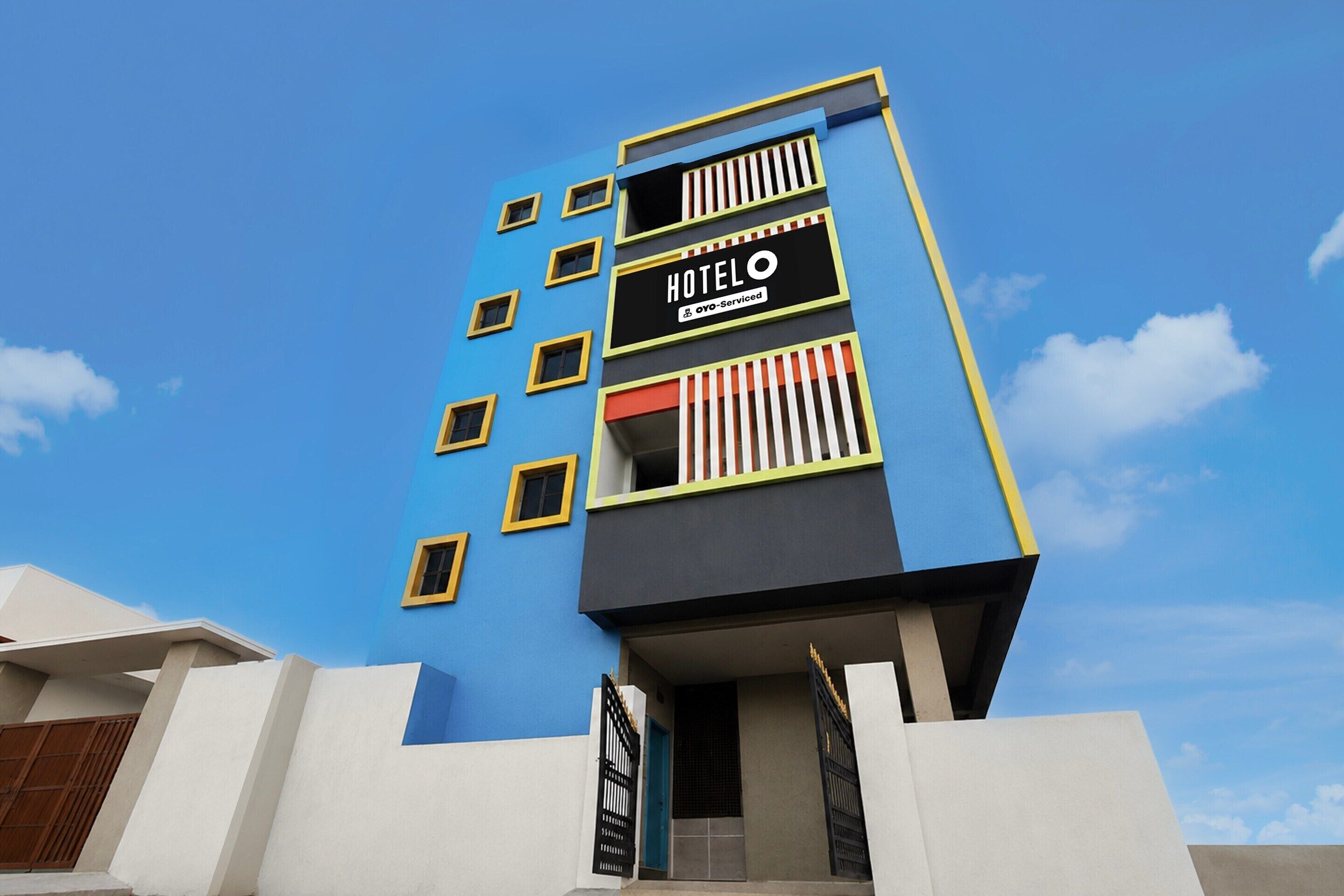 A multi-story hotel building with a blue facade, a sign indicating it is serviced by OYO, and a gated entrance.