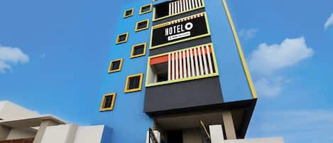 A multi-story hotel building with a blue facade, a sign indicating it is serviced by OYO, and a gated entrance.