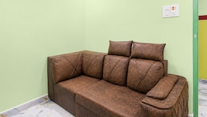 Um sofá castanho com uma almofada numa sala com paredes verde-claras e chão de mármore.