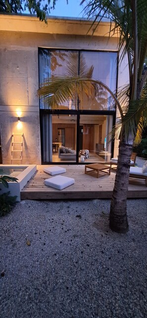 A modern building with a large glass entrance, a pool area with lounge chairs, and a palm tree. - Komorebi House - Episode 6 (Cabarete)