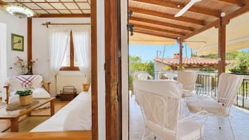 Una stanza con un letto, un tavolo in legno e una sedia. È presente un balcone con sedie bianche e una ventola a soffitto.