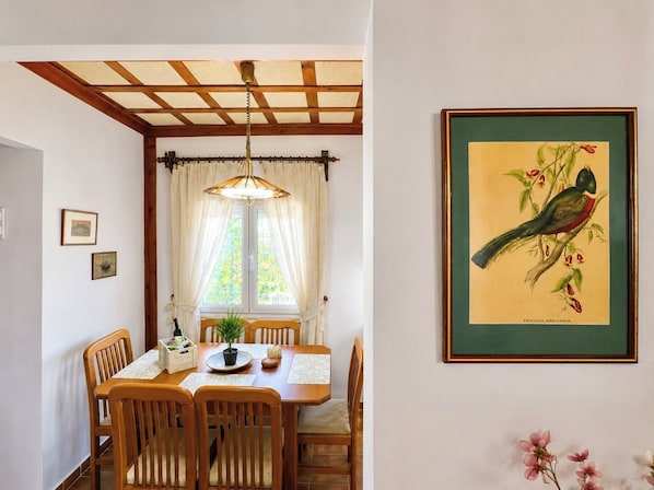 A dining area with a wooden table, chairs, a hanging light fixture, and a framed botanical illustration on the wall.