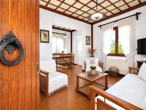 A room with a bed, a wooden chair, a table, a TV, and a window with curtains.