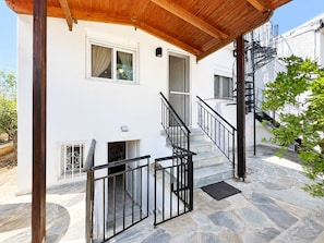 Ein zweigeschossiges Gebäude mit einer flach gedeckten Steinveranda, einer Holzpergola und einer Wendeltreppe.
