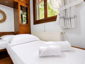 A bedroom with two beds, a window with curtains, a radiator, and a wooden wardrobe.