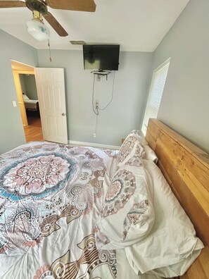 A bedroom with a bed, a ceiling fan, a mounted TV, and a door leading to another room. - Family & pet friendly 3 BDR, walk to restaurants & nightlife in Murray Hill (Jacksonville)
