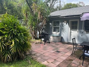Eine Terrassenfläche mit Grill, Esstisch und Stühlen, umgeben von üppiger Bepflanzung.