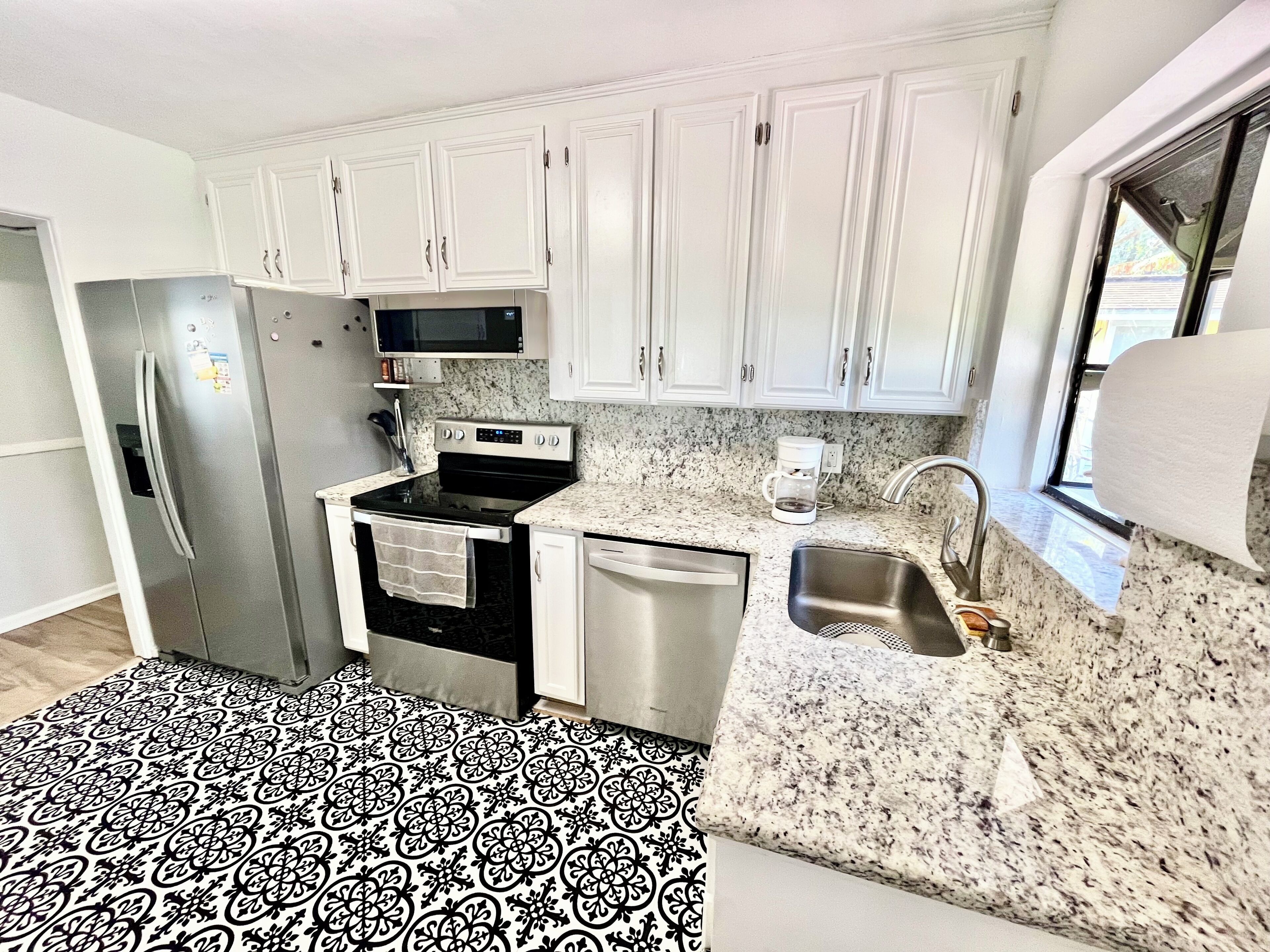 A compact kitchen with white cabinets, a stainless steel refrigerator, a microwave, an oven, and a dishwasher.