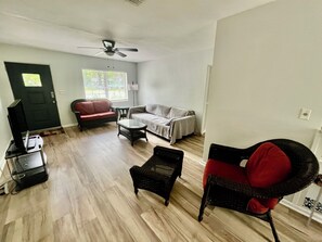 A living room with a ceiling fan, a red sofa, a grey sofa, a coffee table, and a black chair. - Family & pet friendly 3 BDR, walk to restaurants & nightlife in Murray Hill (Jacksonville)