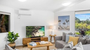 A modern living room with a flat-screen TV, a sofa, a coffee table, and a potted plant. - Belmore Palms Sunshine Beach (Sunshine Beach)