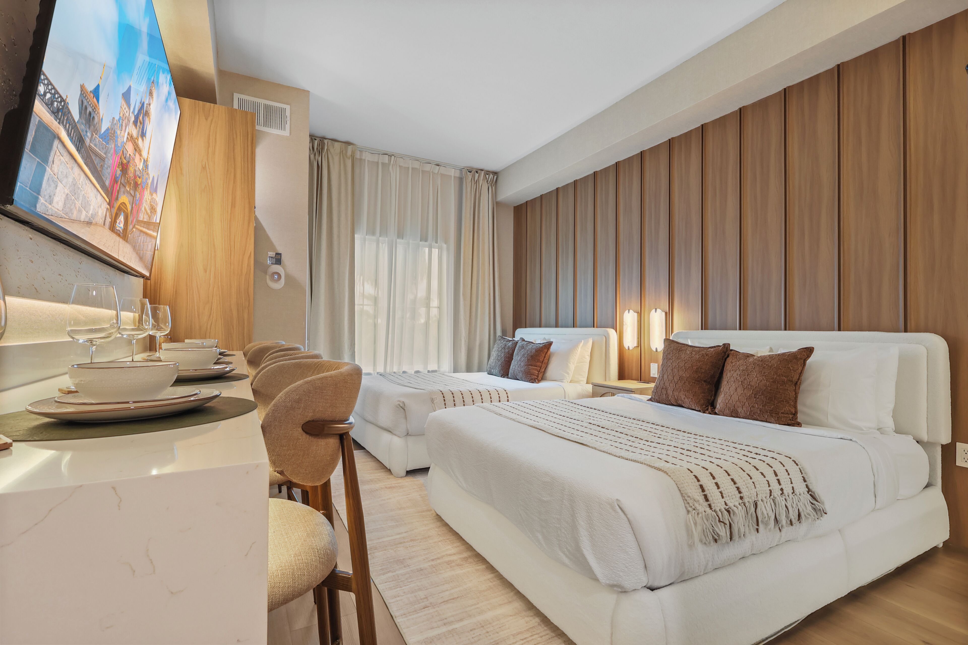 A hotel room with a bed, a desk with a chair, a TV, and a window with curtains.