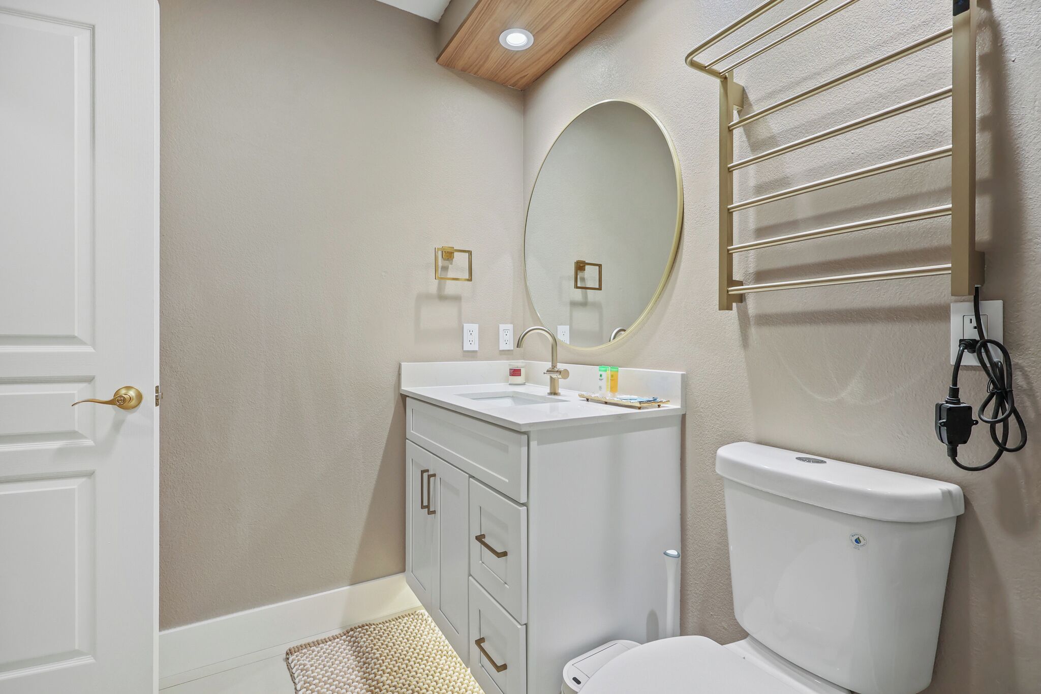Ein Badezimmer mit Toilette, Waschbecken und Spiegel. An der Wand ist ein Handtuchhalter angebracht und eine Tür mit Griff.