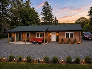 A two-story log cabin with a porch, a red sofa, and a car parked in the driveway. - Charming Sewickley Retreat close to Pittsburgh with Hot Tub (Sewickley)