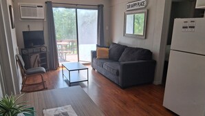 A living room with a sofa, a small table, a TV, and a sliding glass door leading to an outdoor area.