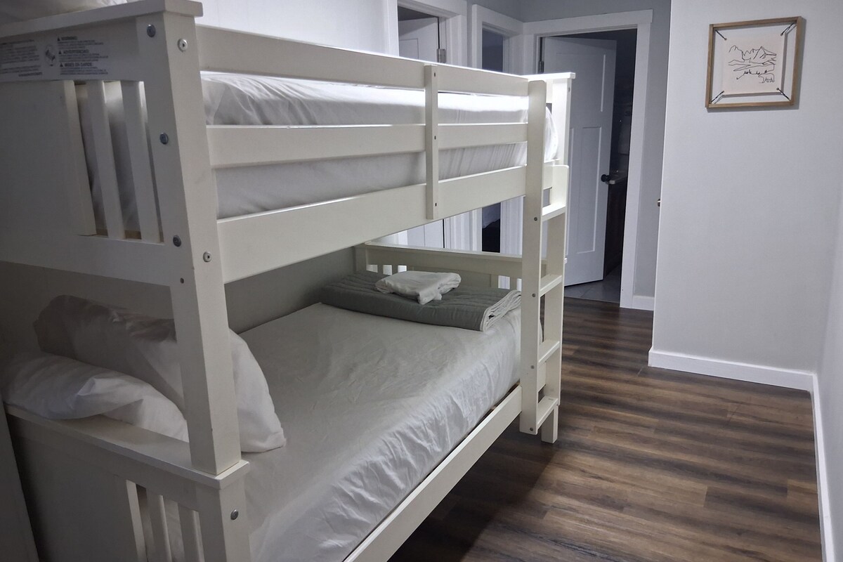 A bunk bed with a lower bunk and a single bed, a wooden floor, a door, and a framed picture on the wall.