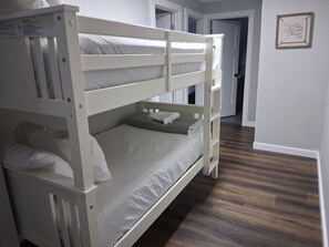 A bunk bed with a lower bunk and a single bed, a wooden floor, a door, and a framed picture on the wall. - Kimberling Cove Resort (Kimberling City)