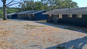 A row of single-story buildings with a gravel driveway and trees in the background.