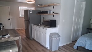 A compact kitchen with a refrigerator, microwave, and wooden shelves.
