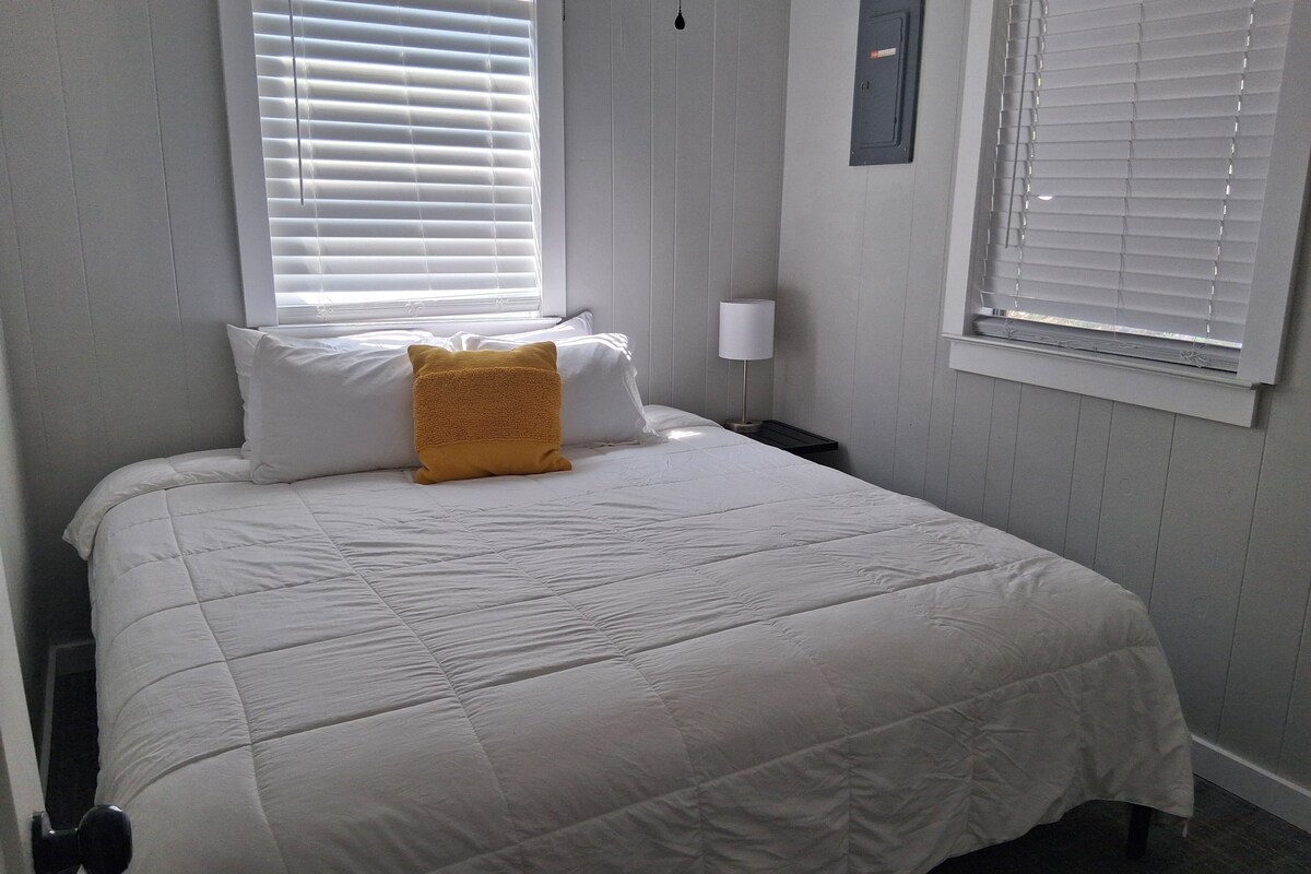 A neatly made bed with a white comforter and a single yellow accent pillow.