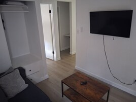 Una sala de estar con un televisor de pantalla plana montado en la pared, una mesa de centro de madera y un sofá con un cojín decorativo.