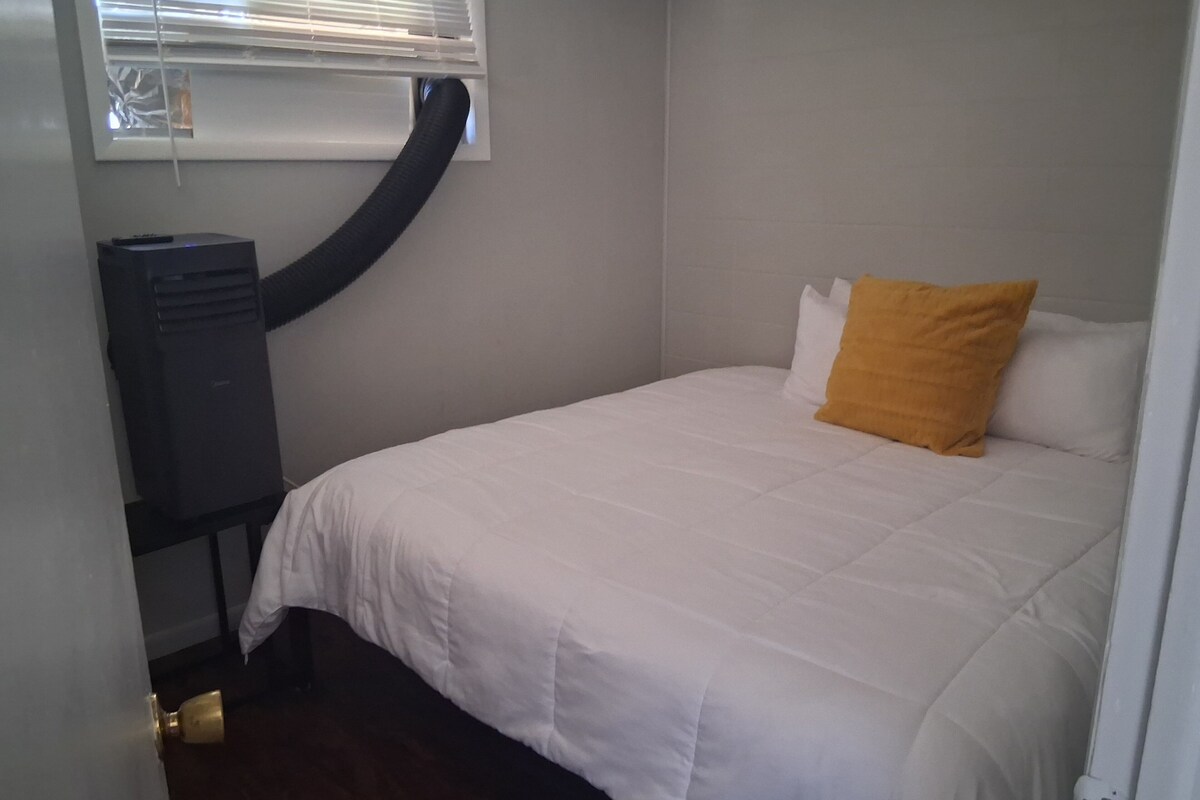 A bedroom with a bed, a window with blinds, a heater, and a door.