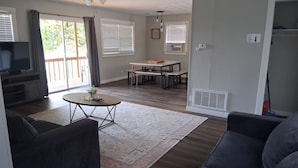 A living room with a sofa, a coffee table, and a television. There is a dining area with a table and chairs.
