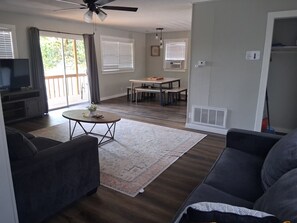 A living room with a sofa, a coffee table, and a television. There is a dining area with a table and chairs. - Kimberling Cove Resort (Kimberling City)
