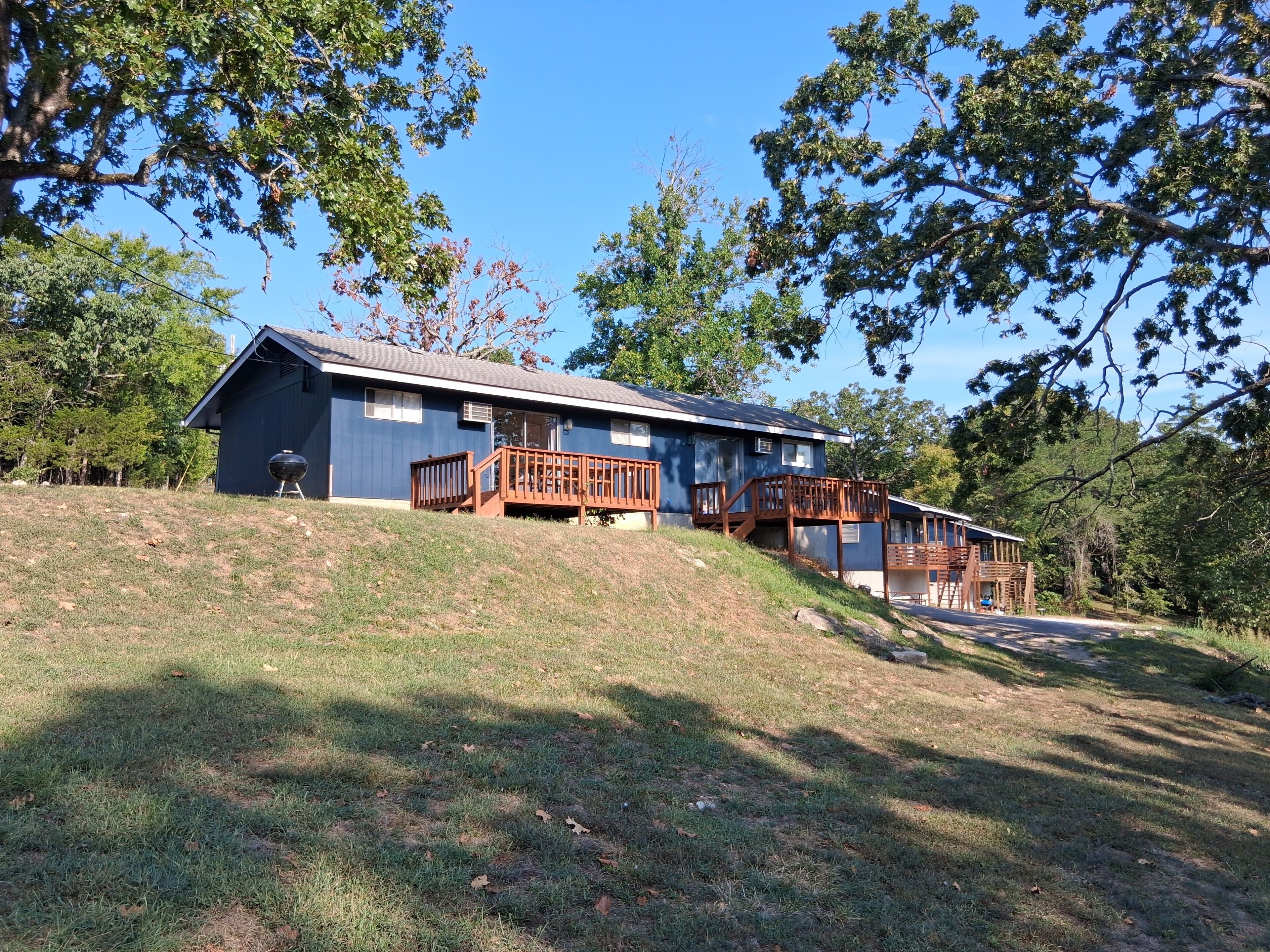 A two-story cabin with a deck and stairs, surrounded by trees.