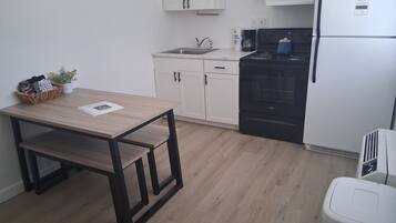 A compact kitchen with white cabinets, a black stove, a white refrigerator, and a small trash bin.