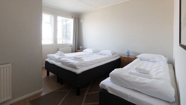Et hotelværelse med to senge, et vindue, en radiator og et lille bord med en lampe.
