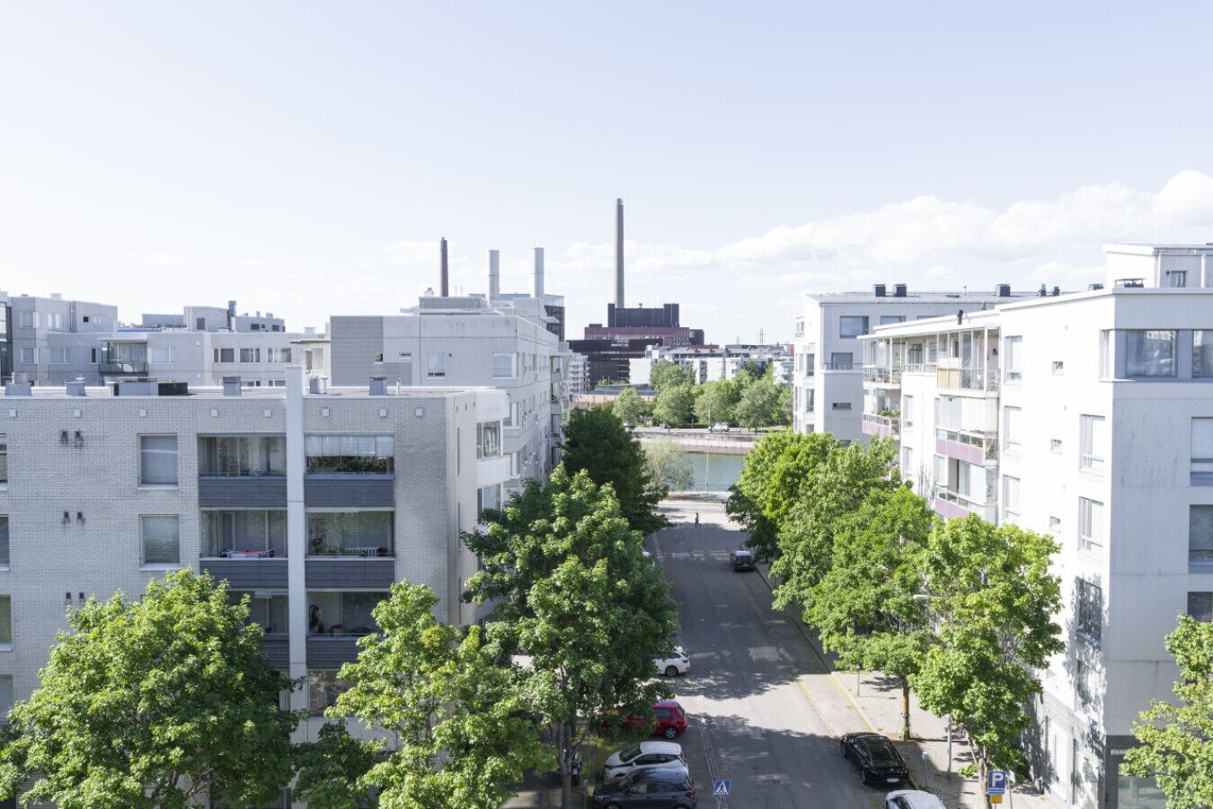 Zona residencial con modernos edificios de apartamentos, una calle con autos estacionados y un río al fondo.